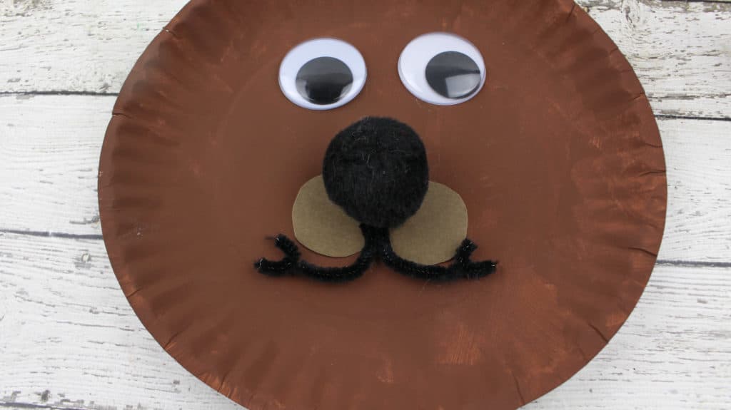 2.   For the nose, generously apply glue to the back of the pom-pom and attach to the paper plate.   3.   Apply glue to the back of the two nickel-size brown circles and place underneath the pom pom nose, side by side.